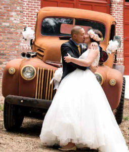 Bride and groom kissing in front of old truck.